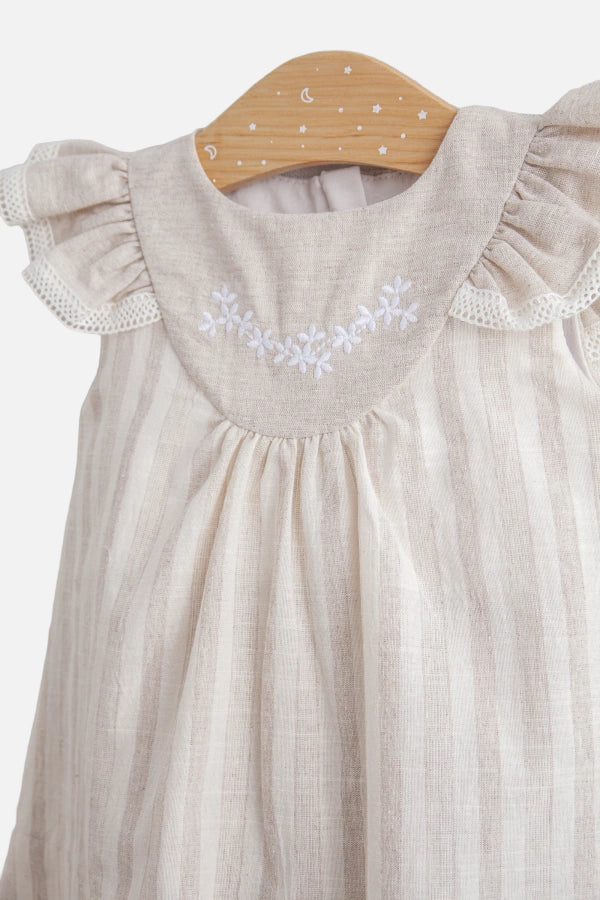 Beige baby dress with floral embroidery on a wooden hanger against a light background
