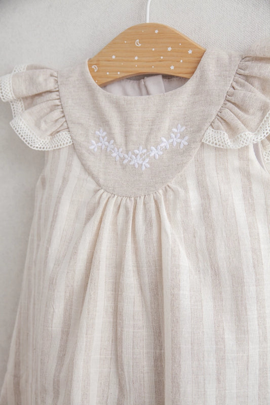 Beige baby dress with floral embroidery on a wooden hanger against a light background