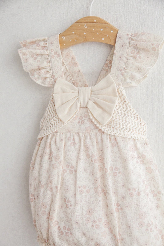 Floral baby romper with a bow on a hanger against a white background