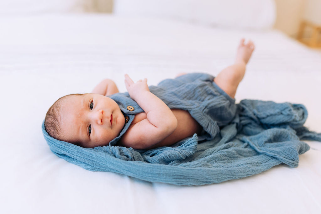 Newborn baby wrapped in a blue blanket on a white surface