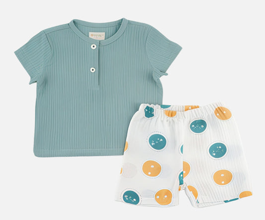 Children's outfit with a green shirt and white shorts with colorful patterns on a light gray background