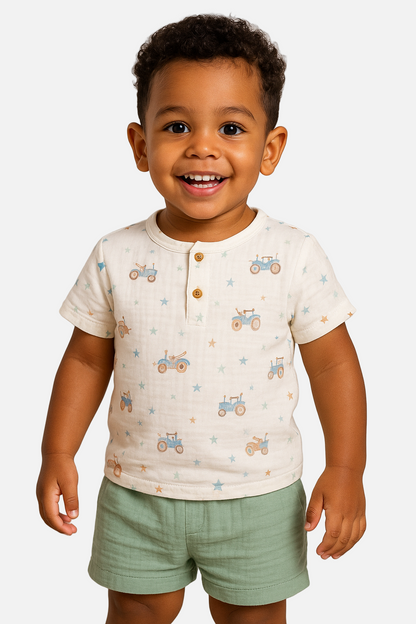 Child wearing a white shirt with vehicle patterns and green shorts on a plain background